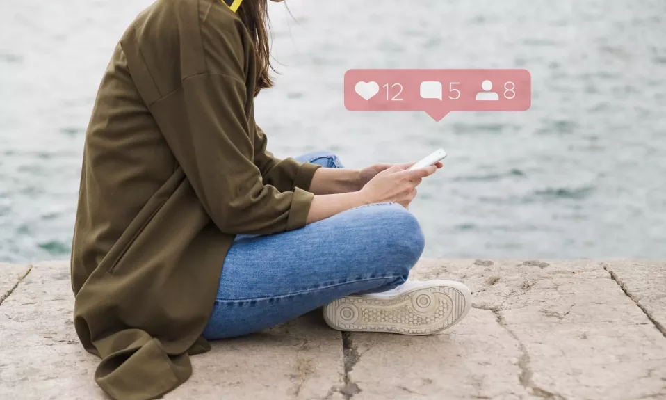 Woman checking smartphone by the sea with social icons.