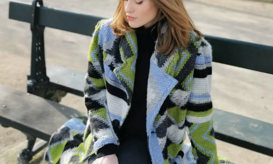 Woman sitting on park bench in colorful coat.